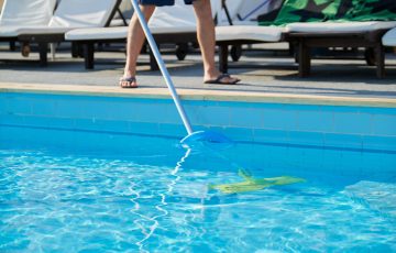 Male cleaning outdoor swimming pool with underwater vacuum tube.